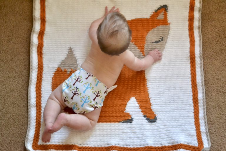 baby laying on belly on a crocheted fox blanket on the floor with a thirsties size two PUL cloth diaper cover